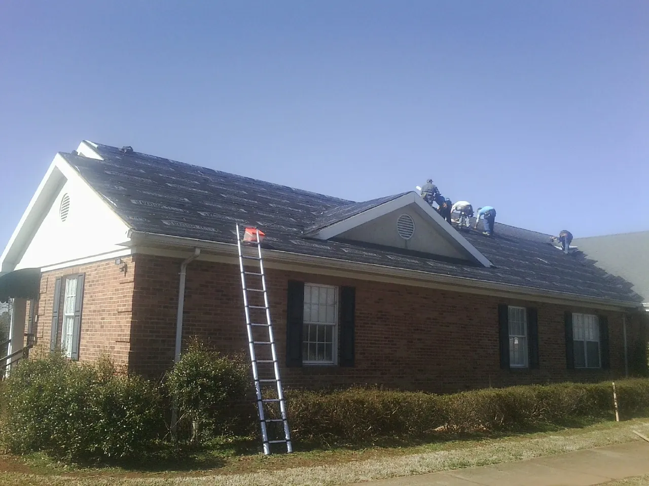 Crew tearing shingles off a brick ranch roof with a ladder set — Emergency Roof Repair work by our crew in Paisley