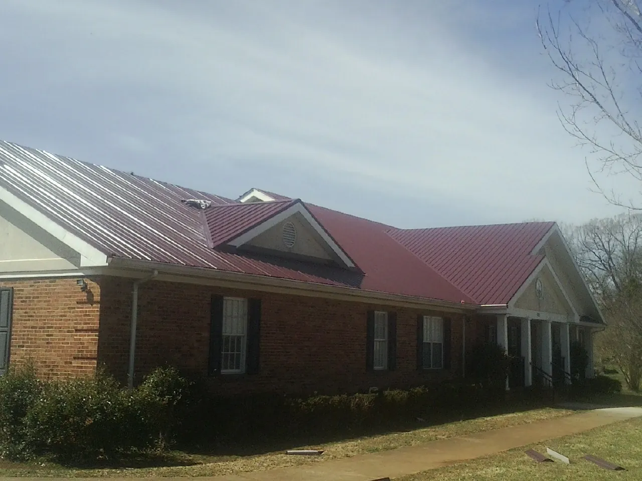 Red metal roof with gabled entries on a long brick building, from a Hail Damage Roof Repair job in Paisley