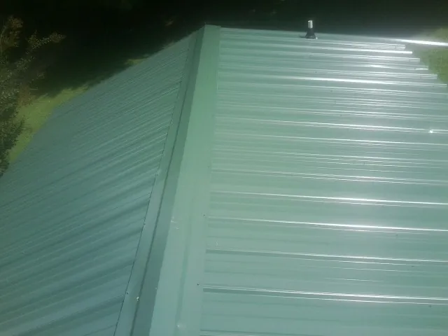 New green metal panels meeting at the ridge of a roof — Flat Roof Repair work by our crew in Paisley
