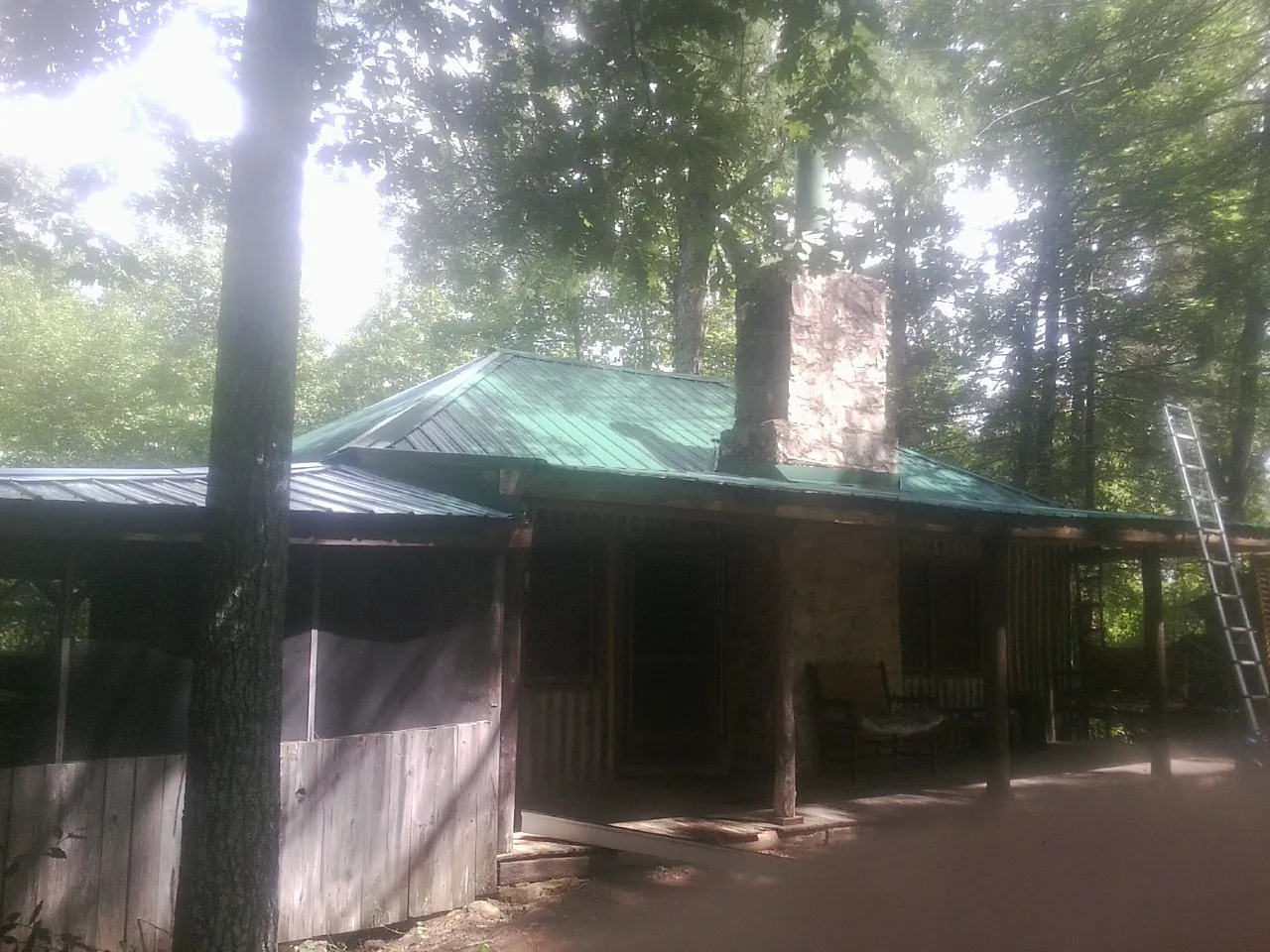 Green metal roof and stone chimney above a log cabin porch in Paisley